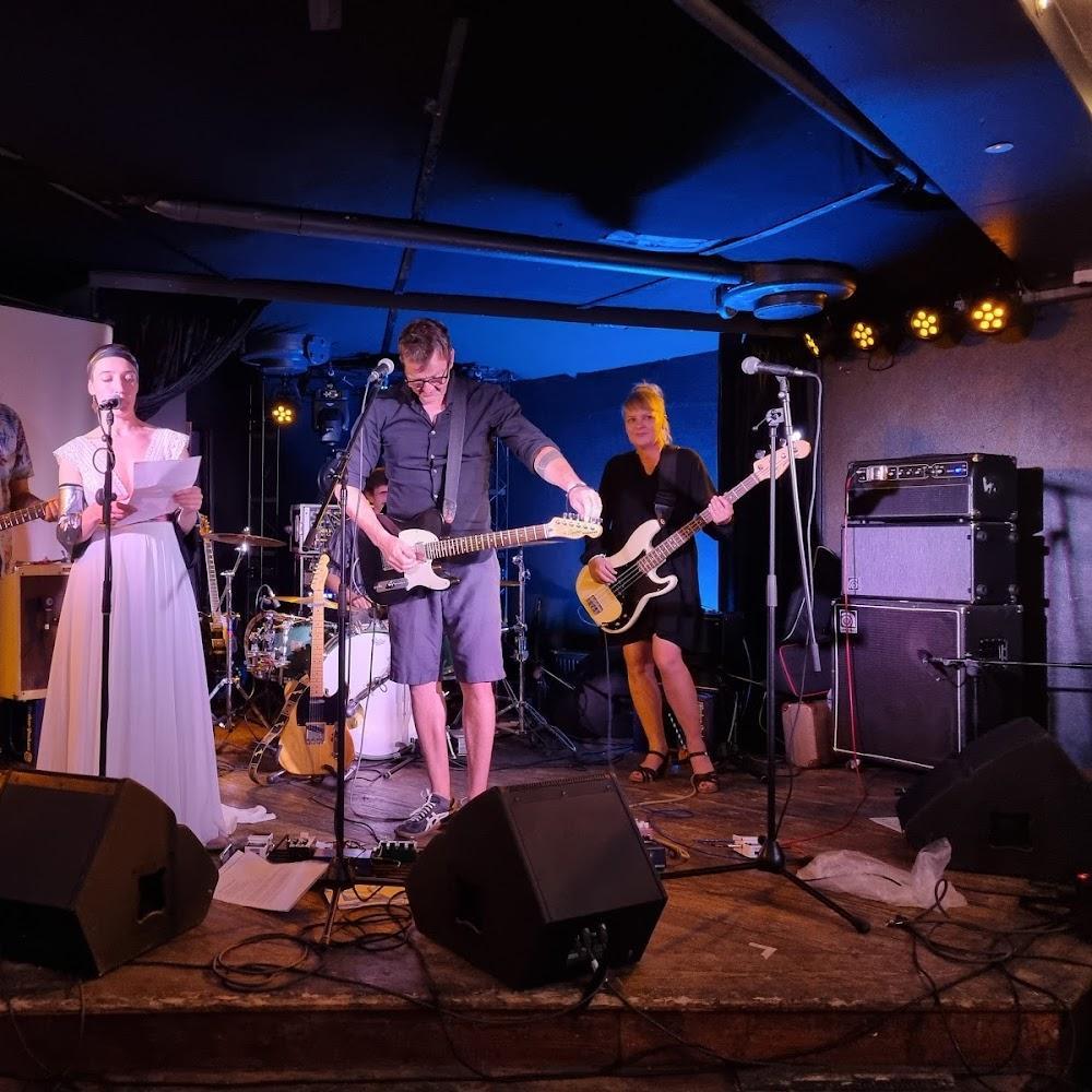 A band is performing on a stage. A woman is singing. A man is playing an electric guitar. A woman is playing a bass guitar.